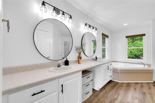full bathroom with double vanity, a sink, a bath, and wood finished floors