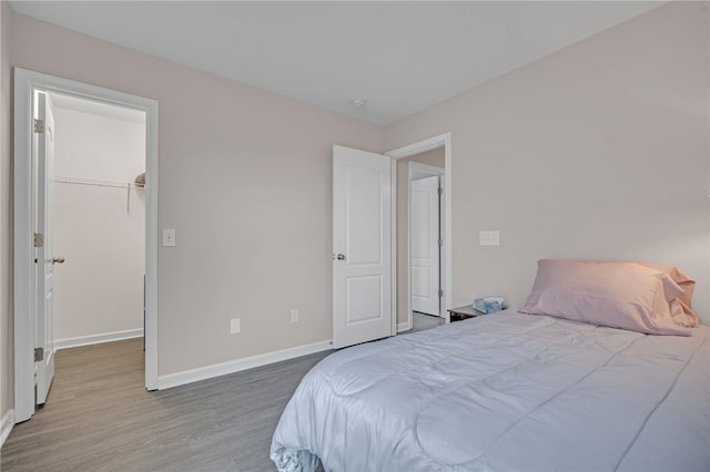 bedroom with a walk in closet, baseboards, and wood finished floors