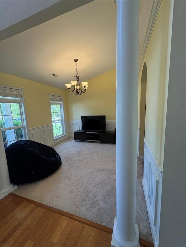 carpeted living area with visible vents, arched walkways, wainscoting, wood finished floors, and an inviting chandelier