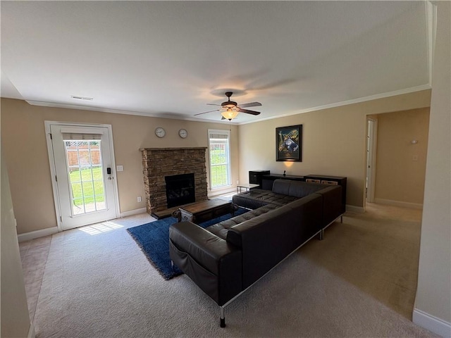 living room featuring ornamental molding, a fireplace, baseboards, ceiling fan, and light colored carpet