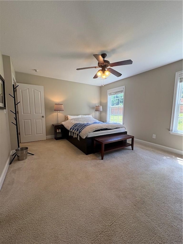 bedroom featuring baseboards, a ceiling fan, light carpet, and multiple windows