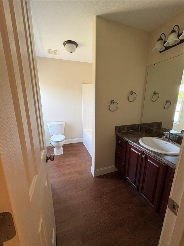 bathroom featuring a bathtub, visible vents, wood finished floors, vanity, and toilet