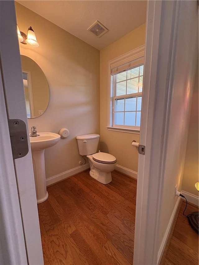 half bath featuring toilet, baseboards, visible vents, and wood finished floors