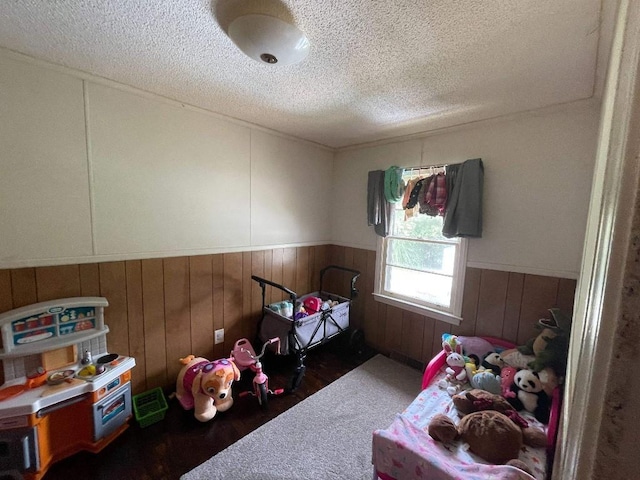 bedroom featuring wooden walls, a textured ceiling, wood finished floors, and a wainscoted wall