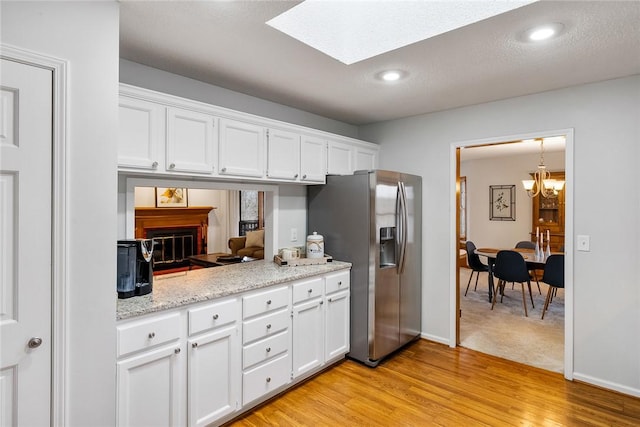 kitchen featuring stainless steel refrigerator with ice dispenser, an inviting chandelier, white cabinetry, and light wood-style flooring