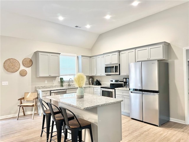 kitchen with light stone counters, a breakfast bar area, stainless steel appliances, a kitchen island, and visible vents