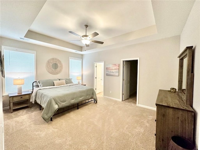 bedroom with a ceiling fan, light colored carpet, visible vents, baseboards, and a tray ceiling