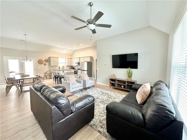 living room featuring baseboards, light wood finished floors, lofted ceiling, and ceiling fan with notable chandelier