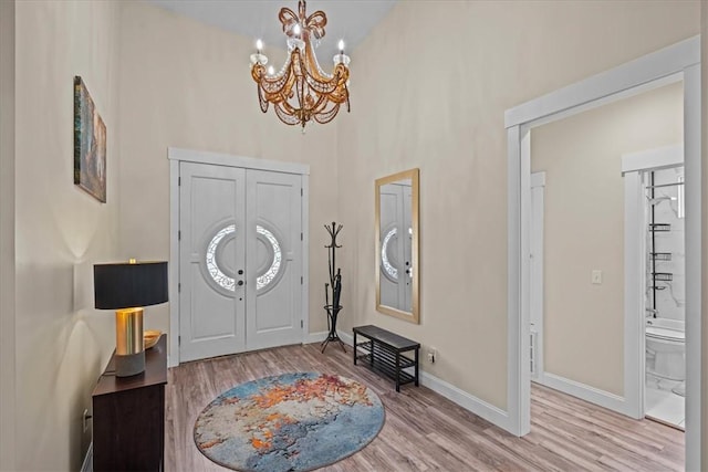 foyer featuring baseboards, a towering ceiling, wood finished floors, and a notable chandelier