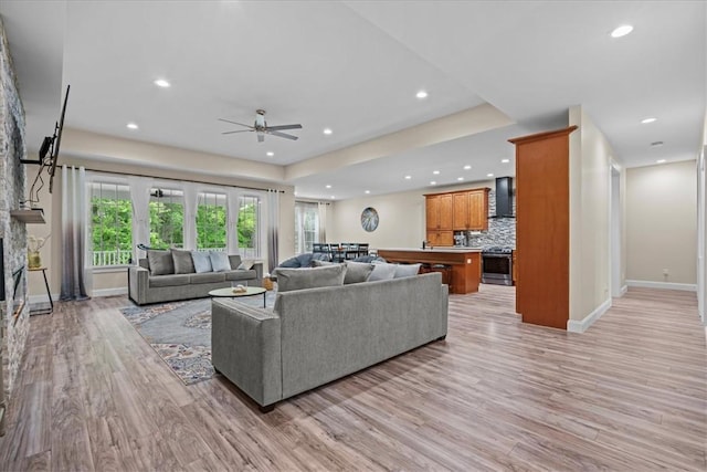 living room featuring a ceiling fan, baseboards, light wood-style floors, a tray ceiling, and recessed lighting