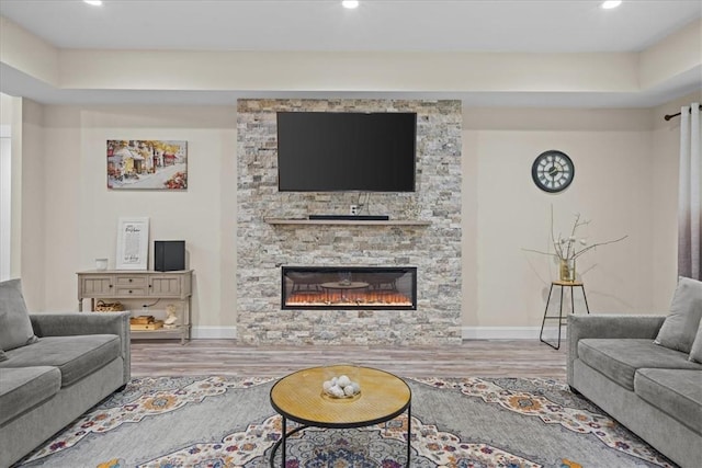 living area featuring recessed lighting, baseboards, a stone fireplace, and wood finished floors