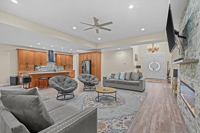 living room with a fireplace, baseboards, recessed lighting, light wood-style flooring, and ceiling fan with notable chandelier