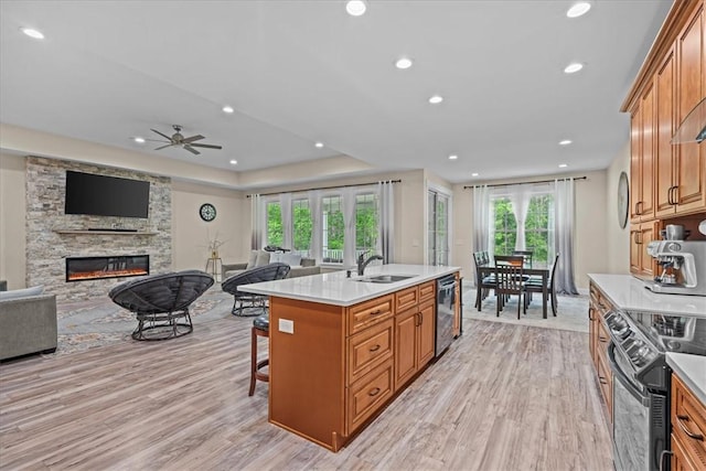 kitchen featuring a stone fireplace, light wood-type flooring, a sink, open floor plan, and black range with electric cooktop