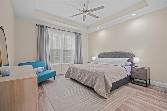 bedroom with a raised ceiling, baseboards, recessed lighting, and wood finished floors