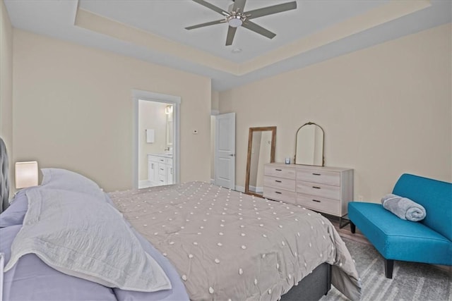 carpeted bedroom featuring a tray ceiling, ceiling fan, and ensuite bath