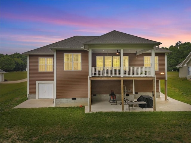 back of property at dusk featuring a ceiling fan, a shingled roof, a patio area, crawl space, and a yard