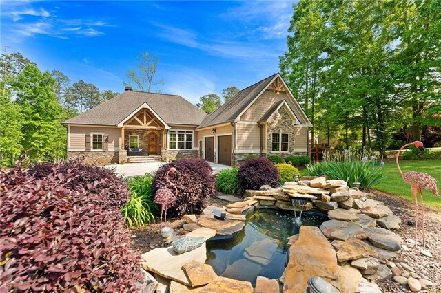 back of house featuring concrete driveway, an attached garage, a small pond, and stone siding