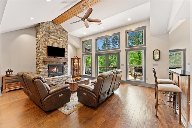living area featuring ceiling fan, a stone fireplace, wood-type flooring, and high vaulted ceiling