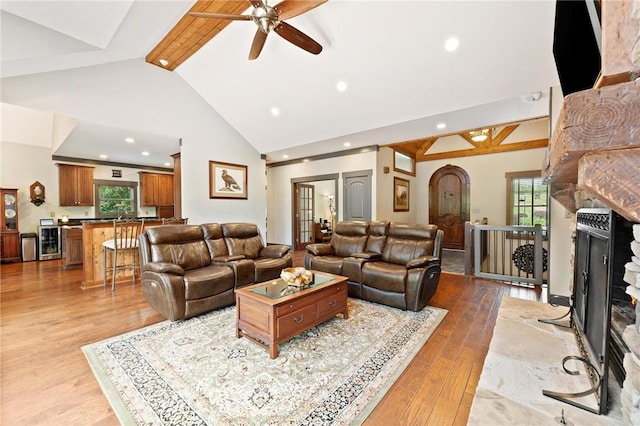 living room with plenty of natural light, ceiling fan, a large fireplace, high vaulted ceiling, and light wood-style flooring