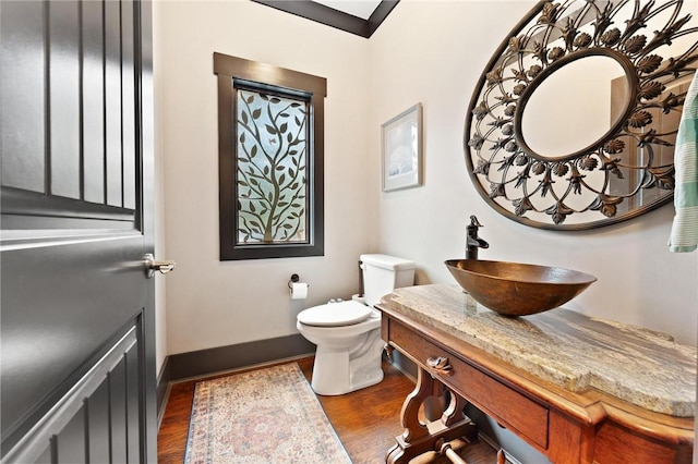 half bathroom featuring vanity, toilet, baseboards, and wood finished floors