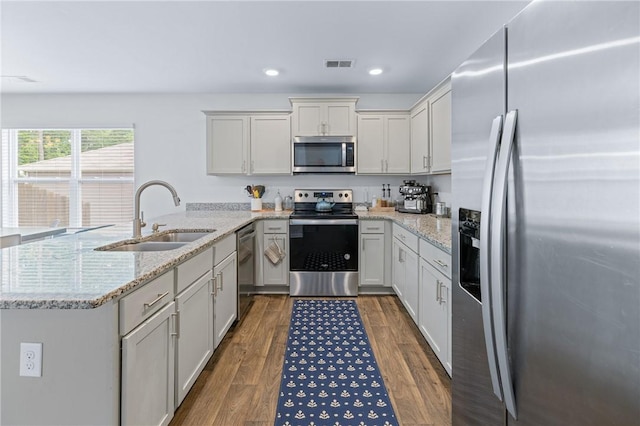 kitchen featuring a peninsula, a sink, stainless steel appliances, visible vents, and dark wood-type flooring