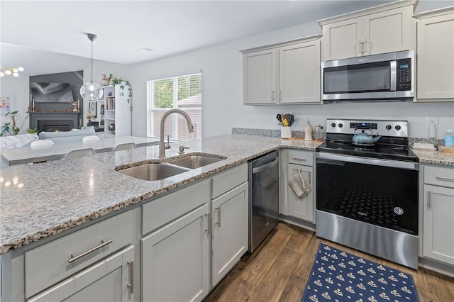 kitchen featuring a sink, a peninsula, stainless steel appliances, light stone counters, and dark wood finished floors