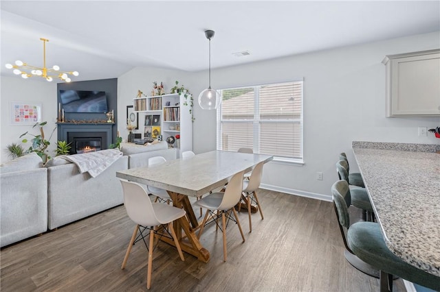 dining space featuring wood finished floors, visible vents, baseboards, a glass covered fireplace, and a chandelier