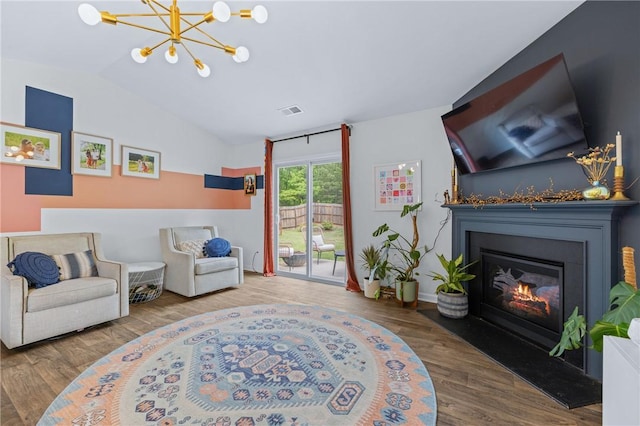 living area with vaulted ceiling, a notable chandelier, a glass covered fireplace, visible vents, and wood finished floors
