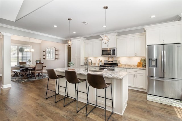 kitchen with a sink, stainless steel appliances, ornamental molding, an island with sink, and white cabinets