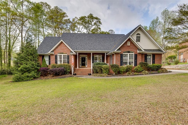view of front of property with covered porch, a shingled roof, brick siding, and a front lawn