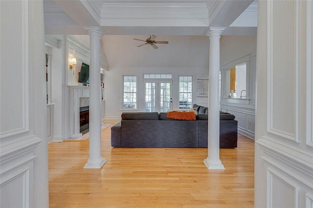 living room with a high end fireplace, light wood-style flooring, ceiling fan, and ornate columns