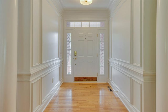 foyer entrance featuring visible vents, a decorative wall, light wood-style flooring, and ornamental molding