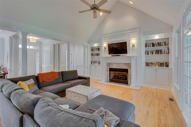 living area featuring high vaulted ceiling, decorative columns, ceiling fan, light wood-style floors, and a fireplace with raised hearth