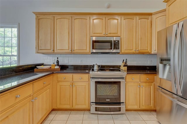 kitchen with tasteful backsplash, light brown cabinetry, dark countertops, and appliances with stainless steel finishes