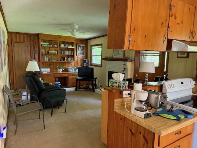 kitchen with brown cabinets, electric stove, light carpet, and ceiling fan