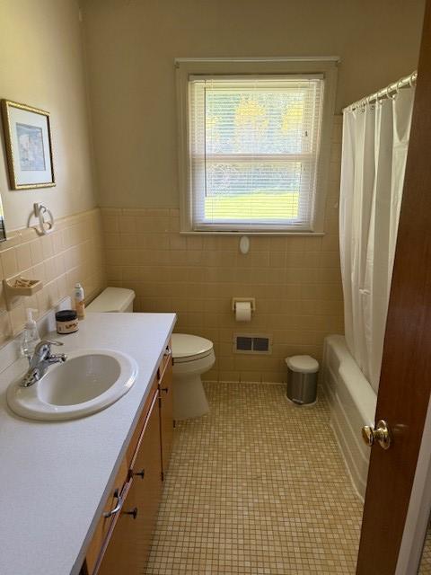 bathroom with toilet, tile walls, visible vents, wainscoting, and vanity