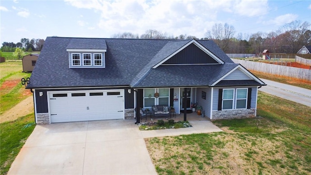 craftsman-style house with driveway, stone siding, a porch, roof with shingles, and a front lawn