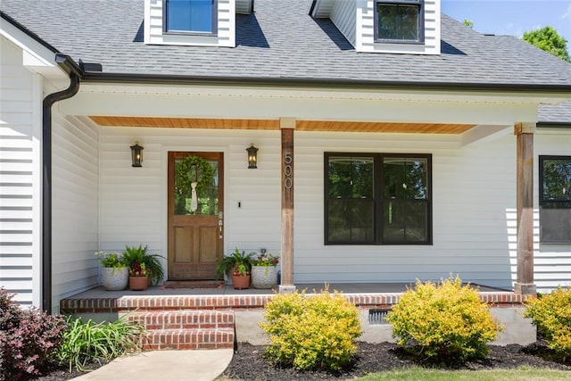 entrance to property with covered porch and a shingled roof