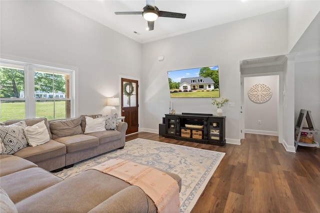 living area featuring a towering ceiling, a ceiling fan, baseboards, wood finished floors, and crown molding