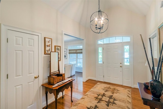 entrance foyer with a chandelier, light wood-type flooring, a towering ceiling, and baseboards