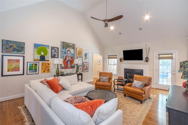 living room featuring high vaulted ceiling, a high end fireplace, light wood-type flooring, baseboards, and a ceiling fan