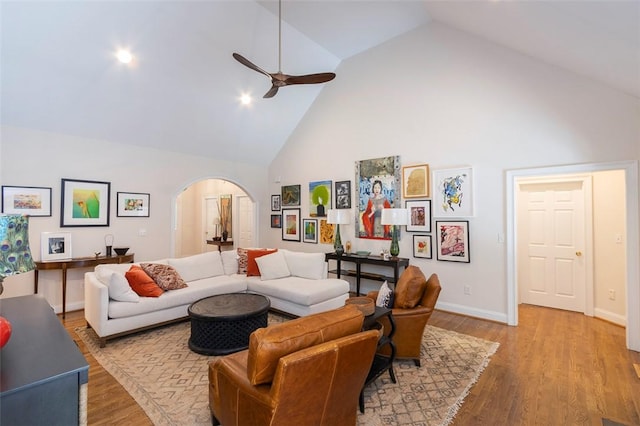 living area featuring high vaulted ceiling, a ceiling fan, arched walkways, light wood finished floors, and baseboards
