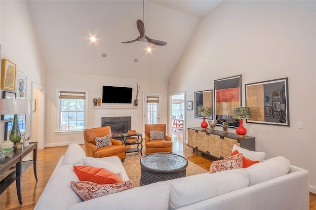 living room with high vaulted ceiling, light wood finished floors, a premium fireplace, a ceiling fan, and baseboards