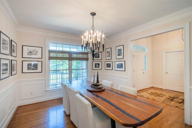 dining space with a chandelier, wood finished floors, ornamental molding, a wainscoted wall, and a decorative wall