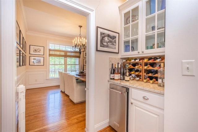 bar with light wood-style flooring, a chandelier, crown molding, and decorative light fixtures