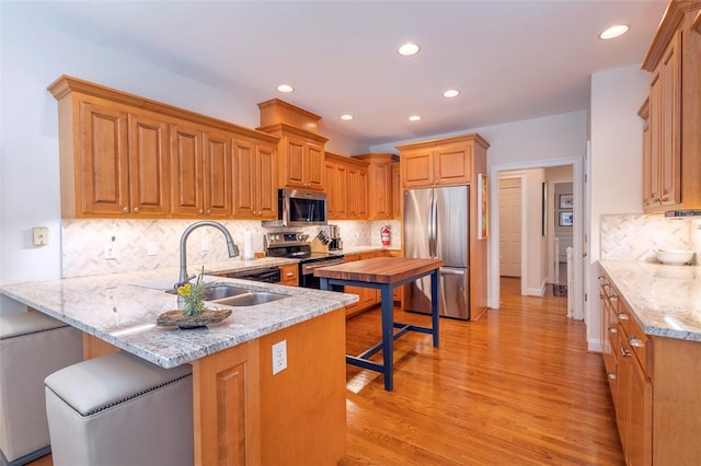 kitchen featuring appliances with stainless steel finishes, a sink, a peninsula, recessed lighting, and light wood-style floors