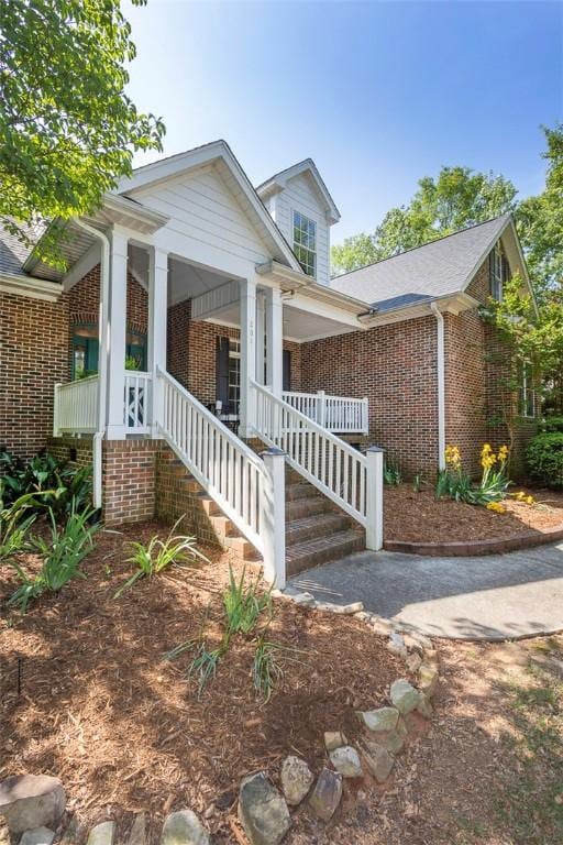 view of front of home with brick siding, covered porch, and stairway