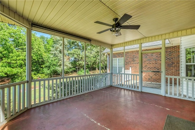 unfurnished sunroom with a ceiling fan and view of scattered trees