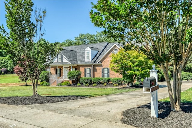 view of front of property with brick siding, covered porch, a front lawn, driveway, and roof with shingles