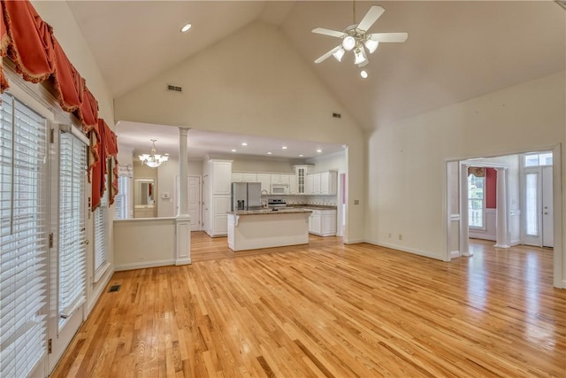 unfurnished living room featuring high vaulted ceiling, a chandelier, light wood-style flooring, ceiling fan, and recessed lighting